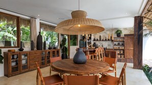 A modern kitchen with a round wooden table, wicker pendant light, and wooden cabinets.