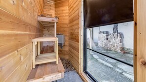 A wooden cabin interior with a small wooden table, a step leading to a loft area, and a window overlooking a stack of bricks outside. - Harry's Handicap Accessible Tea House (Charlotte)