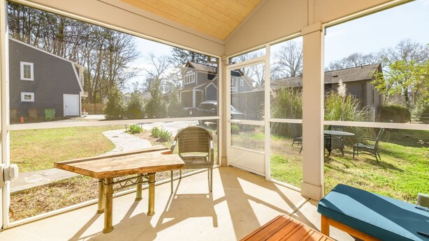 A covered patio with a table and chairs, large windows, and a view of a residential area. - Harry's Handicap Accessible Tea House (Charlotte)