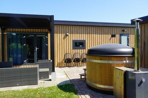 An outdoor seating area with wicker furniture, a wooden barrel, and a modern building with a wooden facade. - Desctription (Waarde)