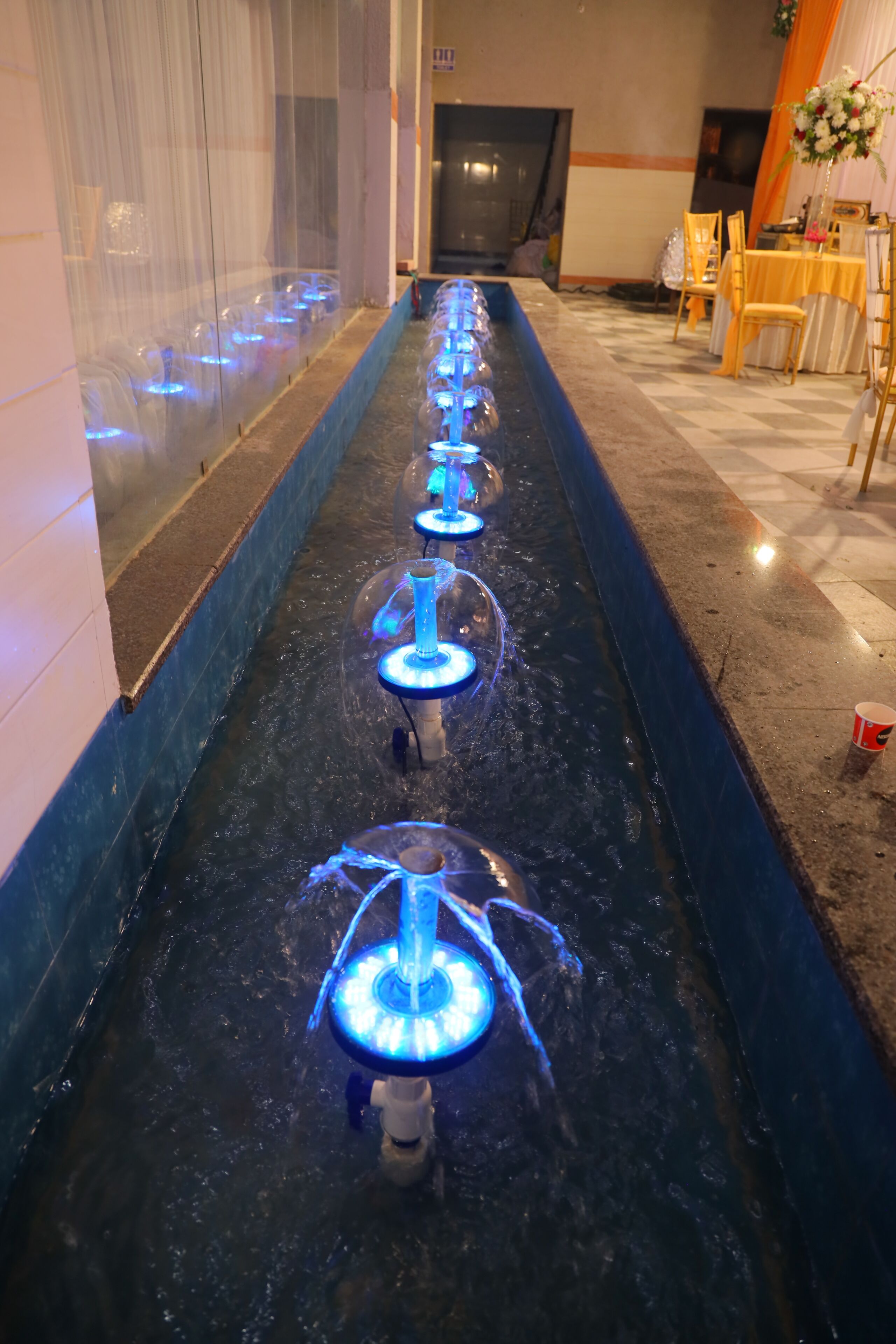 A water feature with illuminated blue lights, a checkered floor, and a table with chairs.