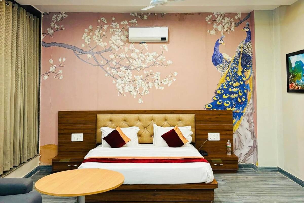 A hotel room with a bed, a round table, a peacock mural, and a ceiling fan.