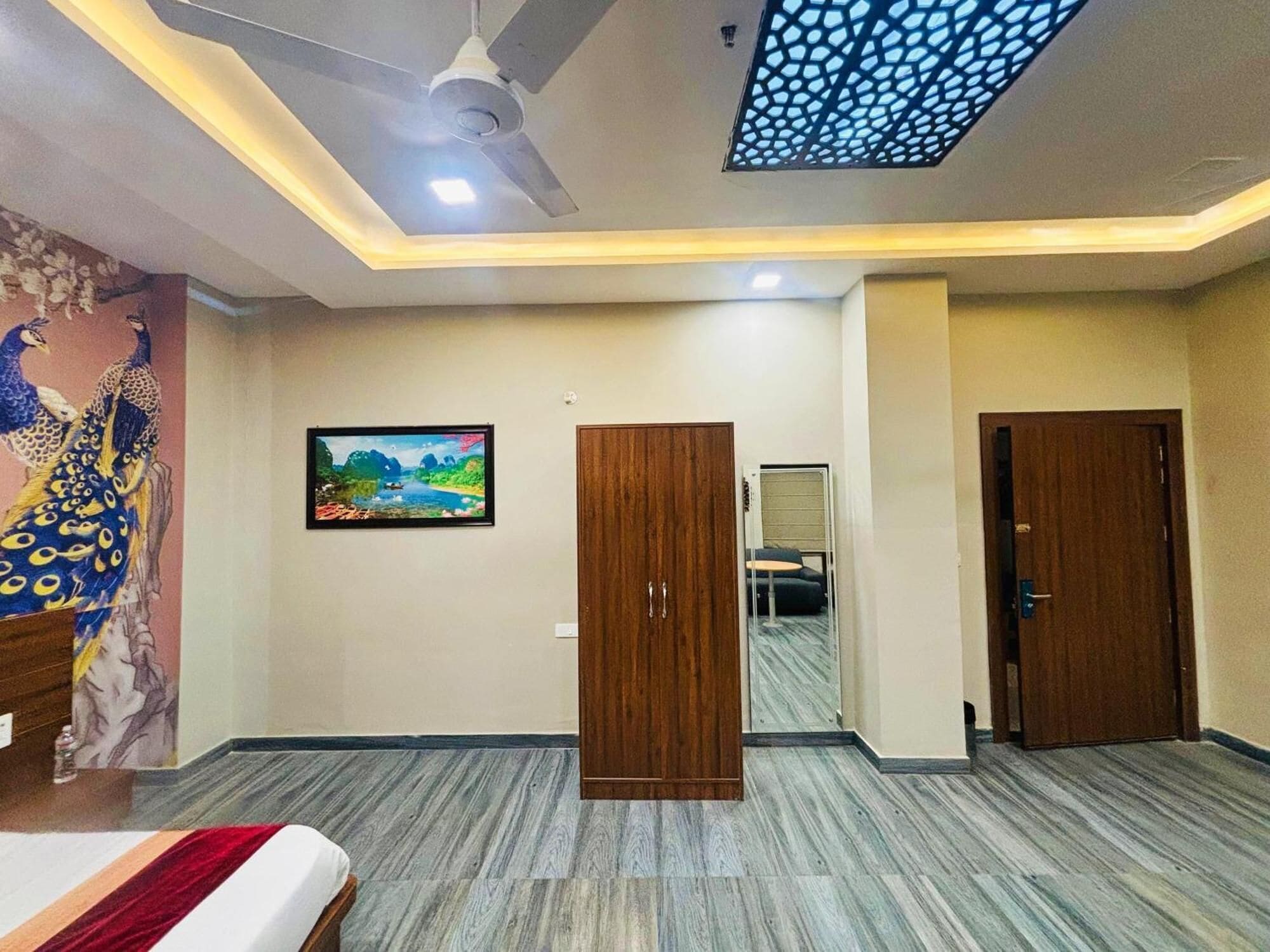 A hotel room with a bed, a ceiling fan, a wooden wardrobe, a door, and a wall-mounted TV.