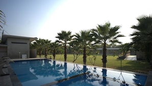 A swimming pool with a tiled deck, surrounded by palm trees and a grassy area.
