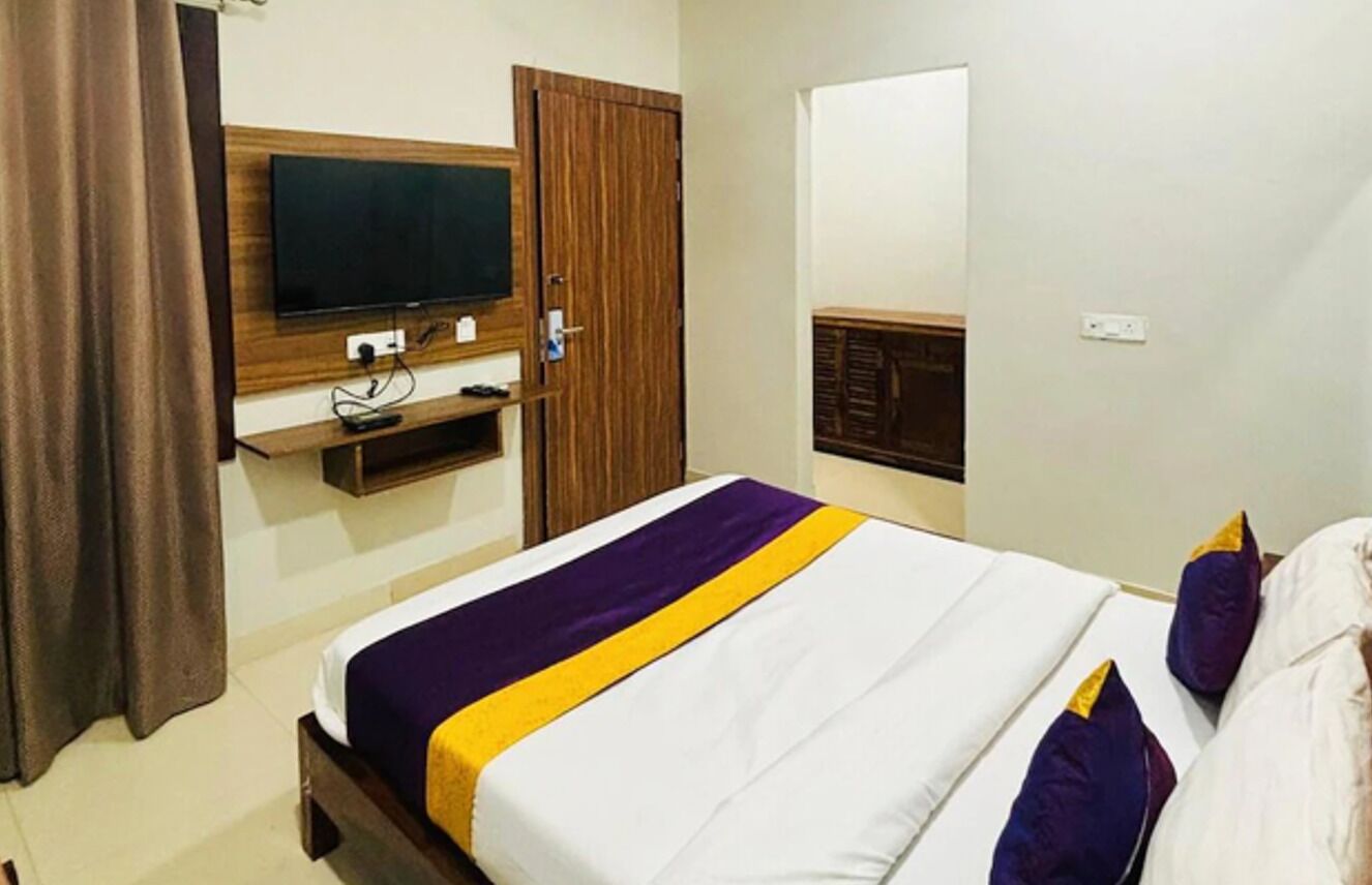 Een hotelkamer met een bed, een aan de muur bevestigde televisie, een houten kast en een deur.