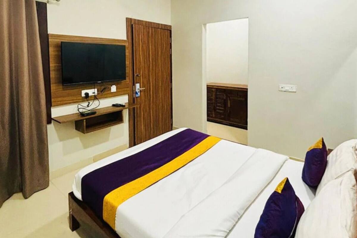 A hotel room with a bed, a television mounted on the wall, a wooden wardrobe, and a door.