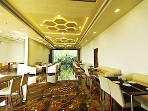 A modern dining area with a marble floor, yellow seating, and a view of greenery through the window.