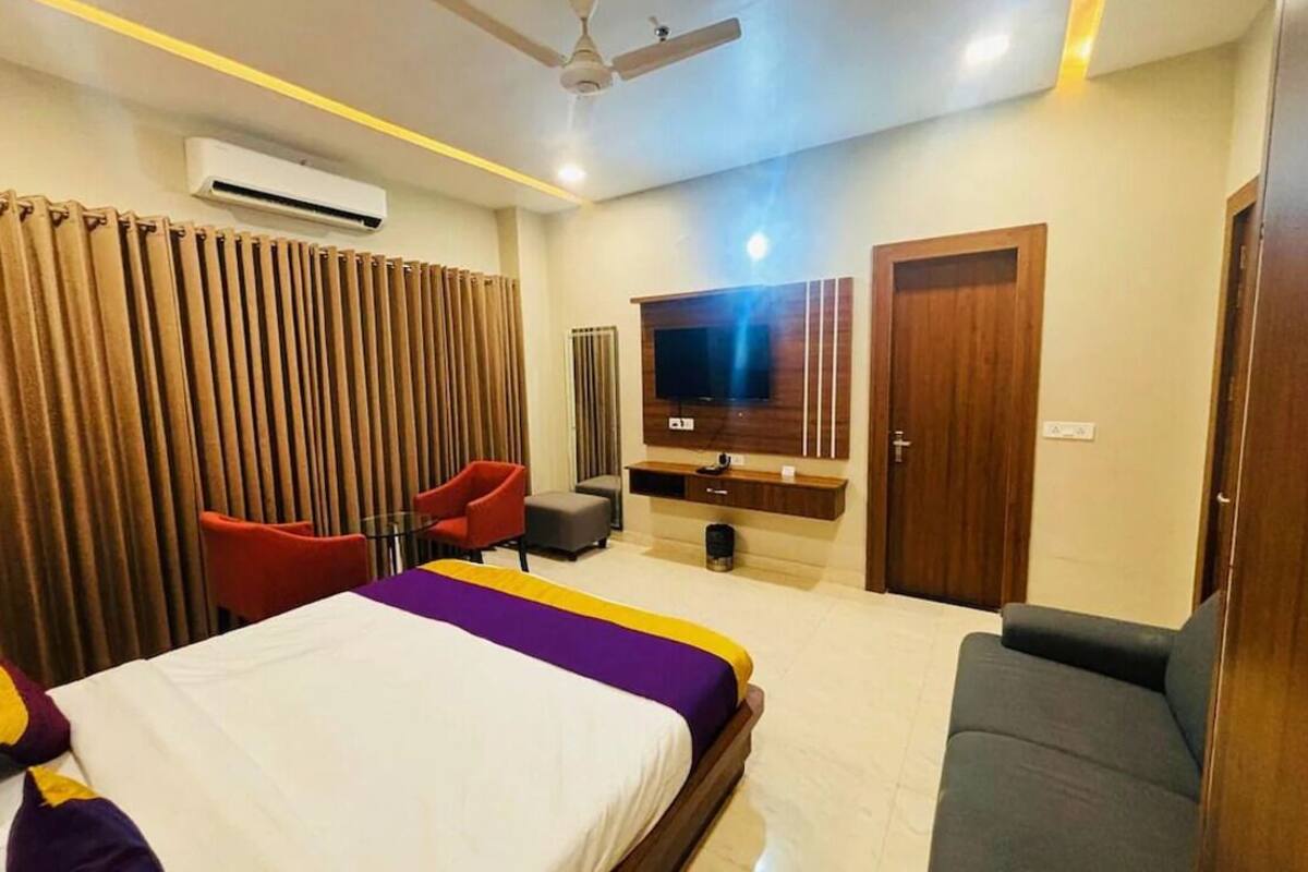 A hotel room with a bed, a TV, a ceiling fan, and a seating area with chairs.