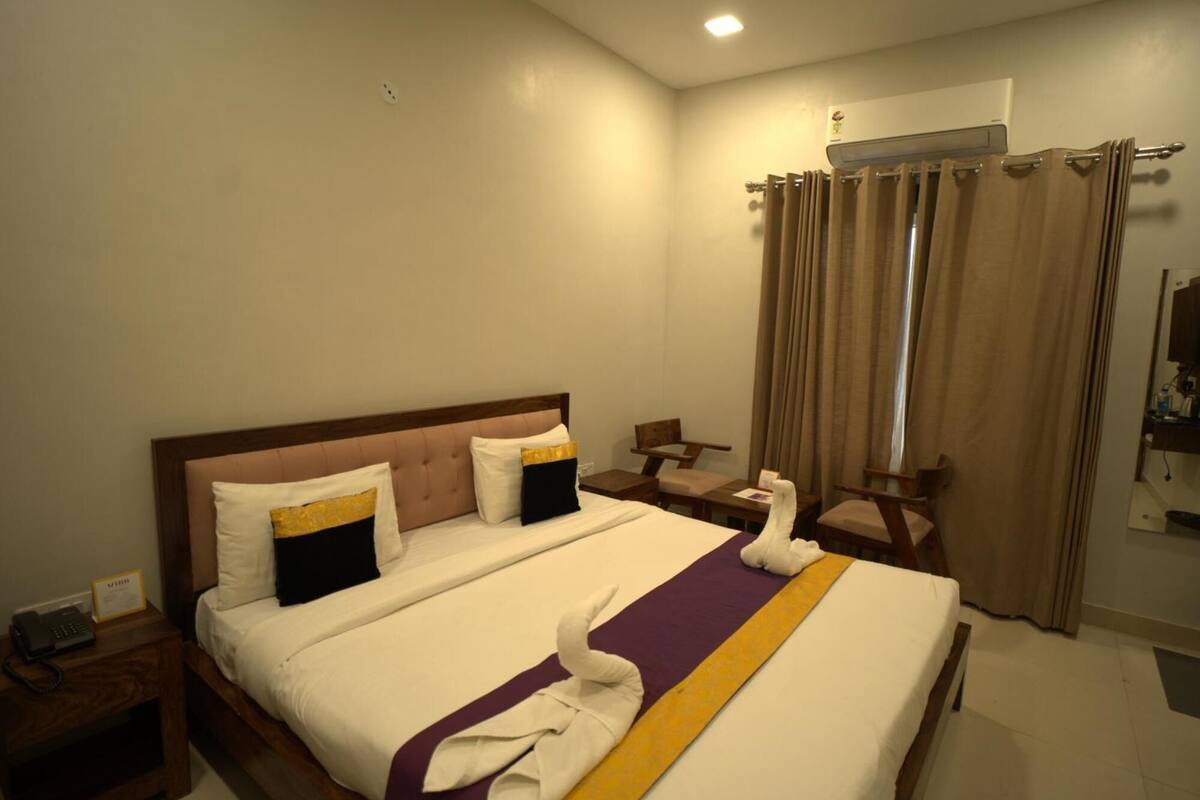 A hotel room with a bed, a desk, a chair, a robe, a telephone, and a curtain.