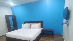 A bedroom with a bed, a nightstand, a TV mounted on the wall, and a ceiling fan. - Hotel Royal Inn (New Delhi)