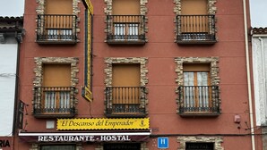 Un edificio rojo con detalles de piedra, varios balcones y un letrero que indica el restaurante y albergue 'El Descanso del Emperador'.