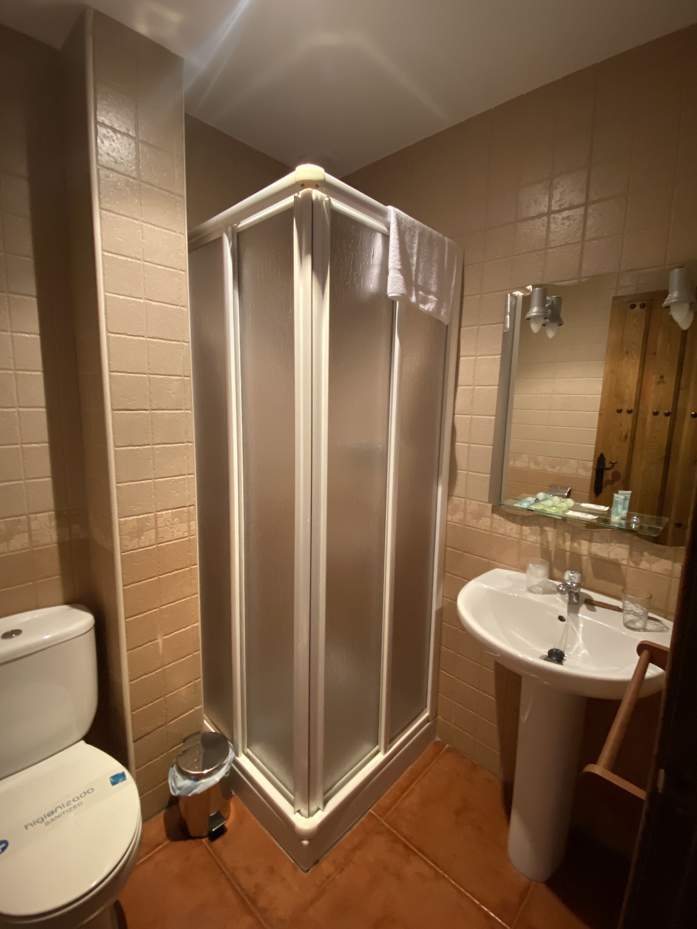 Un baño con cabina de ducha, inodoro, lavamanos y un espejo sobre el lavamanos.