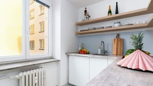Une cuisine moderne avec des meubles blancs, un plan de travail en marbre et une fenêtre donnant sur un immeuble.