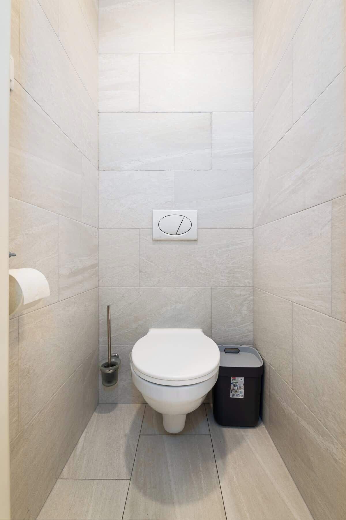 A modern bathroom with a toilet, a trash bin, and a toilet paper holder on the wall.