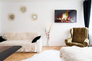 A living room with a white sofa, a brown armchair, a fireplace with a painting above it, and a vase with flowers.