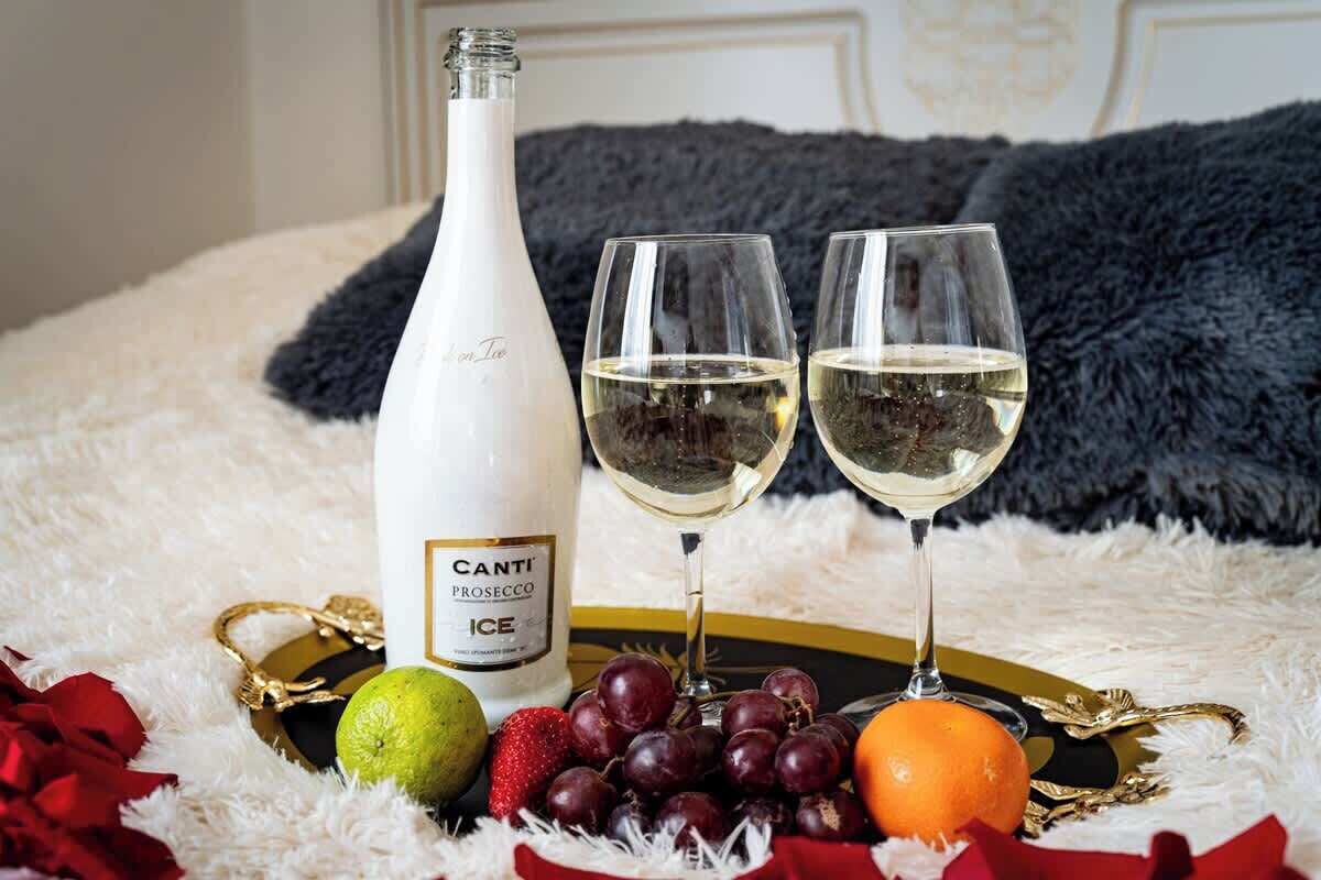 En flaska Canti Prosecco ICE, två glas vin och ett urval av frukter på ett fat.