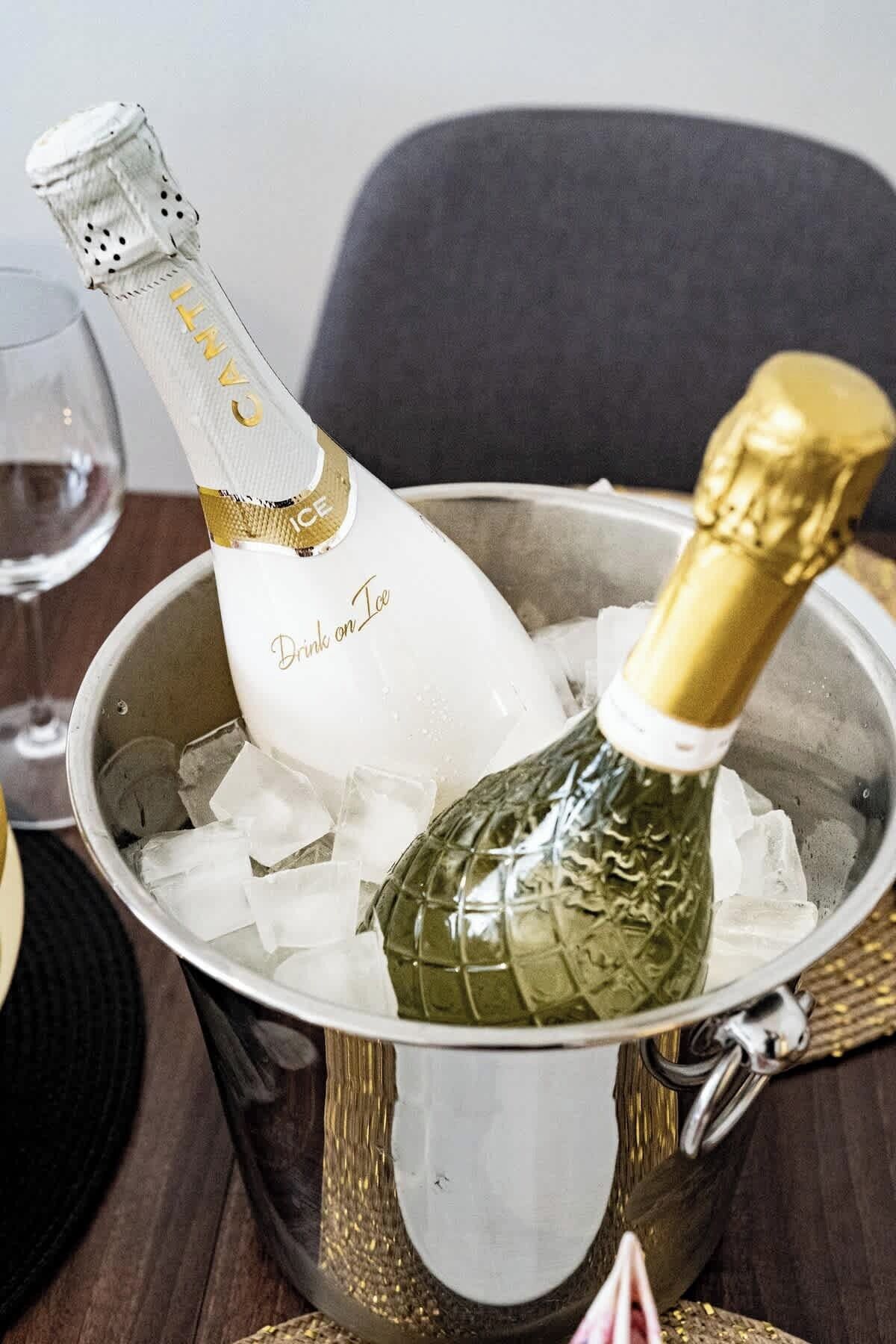 En champagneflaske i en metalspand med is, et glas og en serviet på et bord.