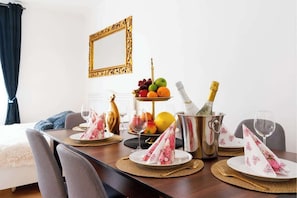 A dining table set with plates, napkins, a fruit bowl, a bottle of champagne, and a decorative vase.