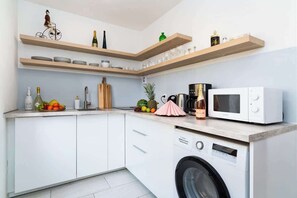 A modern kitchen with white cabinets, wooden shelves, a washing machine, and a microwave.