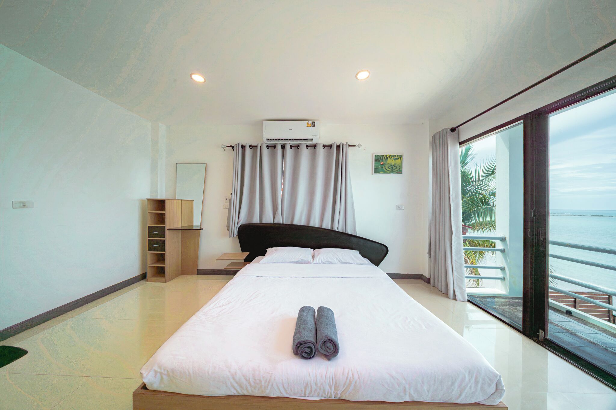 Habitación de hotel con una cama grande, una mesita de noche, un espejo, un armario y vista al mar.