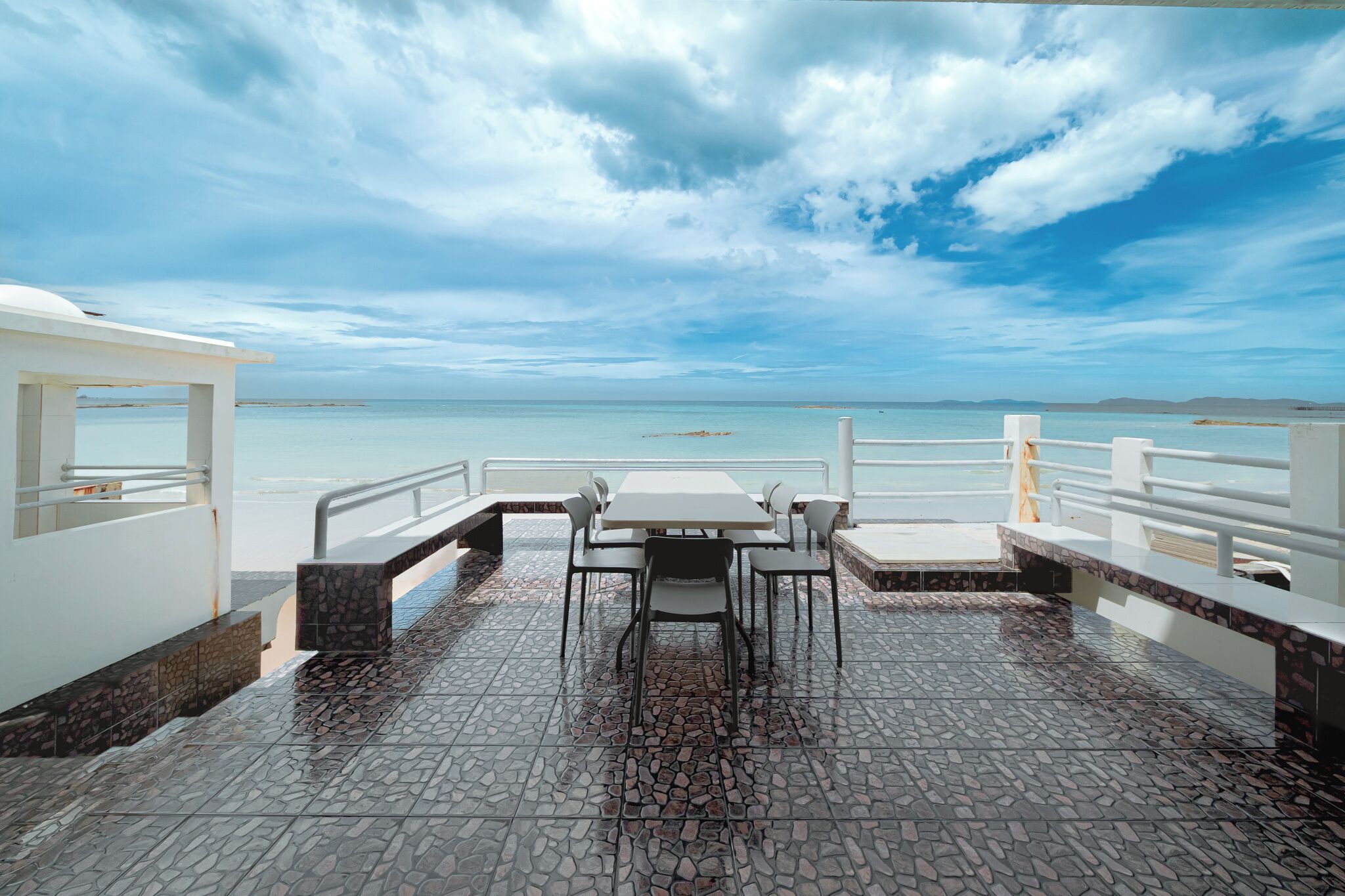 A terrace with a table and chairs, a railing, and a view of the sea.