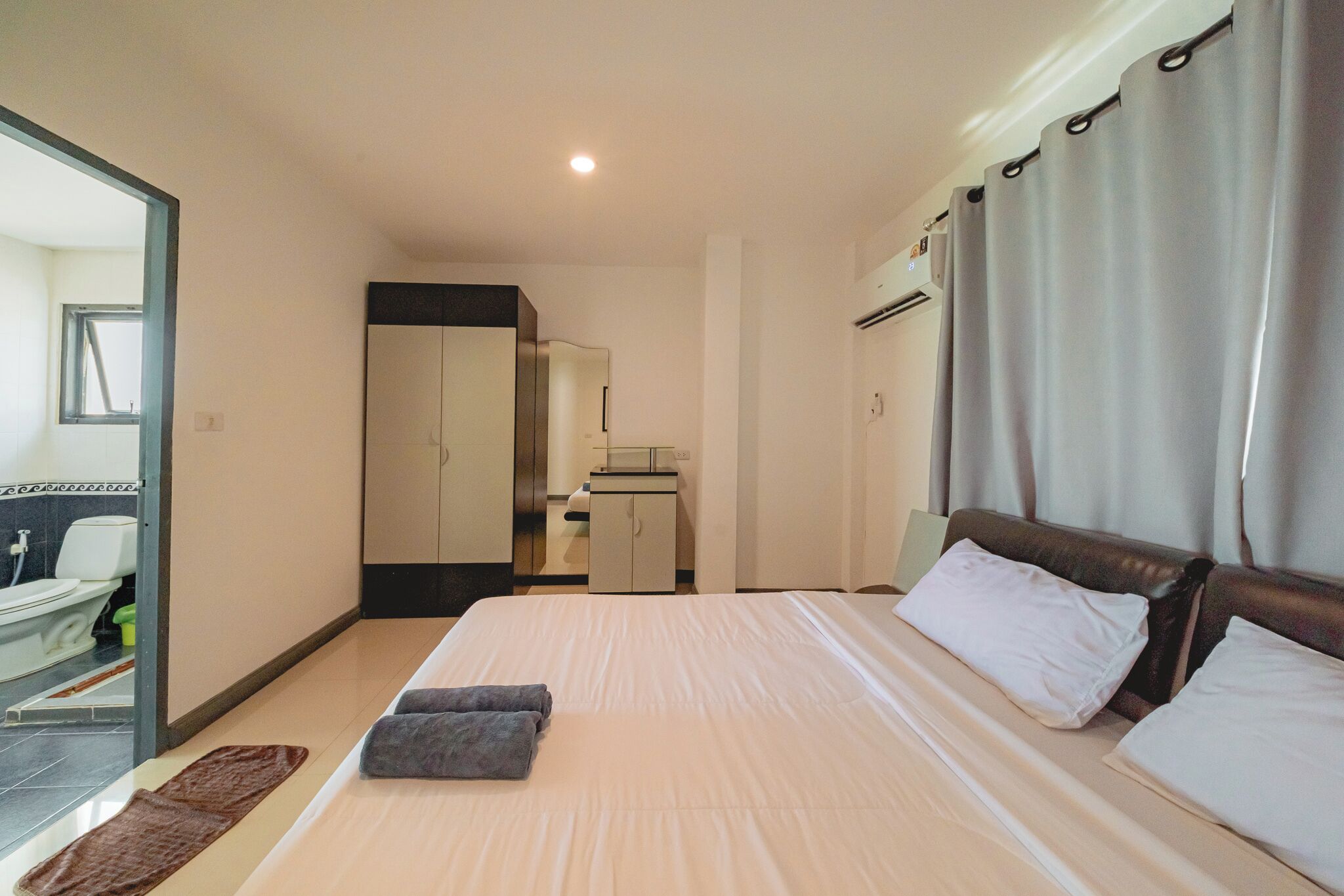 Une chambre d’hôtel avec un lit, un miroir, une armoire, une petite table et une salle de bain à l’arrière-plan.