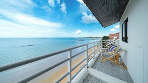 Un balcón con vista al mar, paredes blancas y dos sillas de playa a rayas.