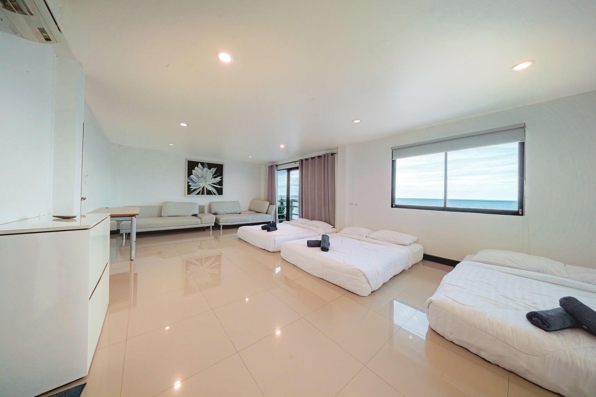 Una habitación de hotel moderna con sofá, dos camas, un escritorio y un ventanal grande.