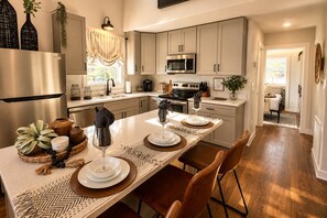 A modern kitchen with a central island, stainless steel appliances, and a dining area with chairs and a table set for two. - Calm Waters at The Retreat at Water's Edge (Tracy City)