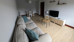 En moderne stue med sofa, fjernsyn, spisebord og et køkkenområde.