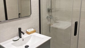 Et moderne badeværelse med en hvid vask, et spejl og en brusekabine med glasvægge.