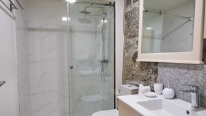 A modern bathroom with a glass-enclosed shower, a toilet, and a sink with a marble countertop.