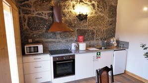A compact kitchen with a stone wall, a microwave, a kettle, a sink, and a coffee machine.