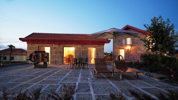 A stone building with a red-tiled roof, outdoor seating, and a barbecue area.