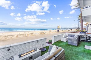 A beachside patio with a fire pit, outdoor furniture, and a lifeguard tower in the background.