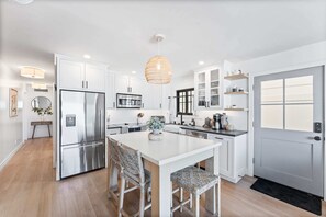 A modern kitchen with white cabinetry, stainless steel appliances, and a central island with bar stools.