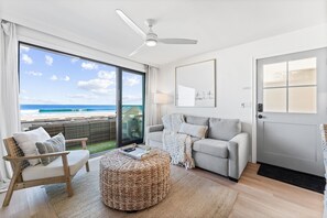 A modern living room with a large sliding glass door leading to a balcony with a view of the ocean.