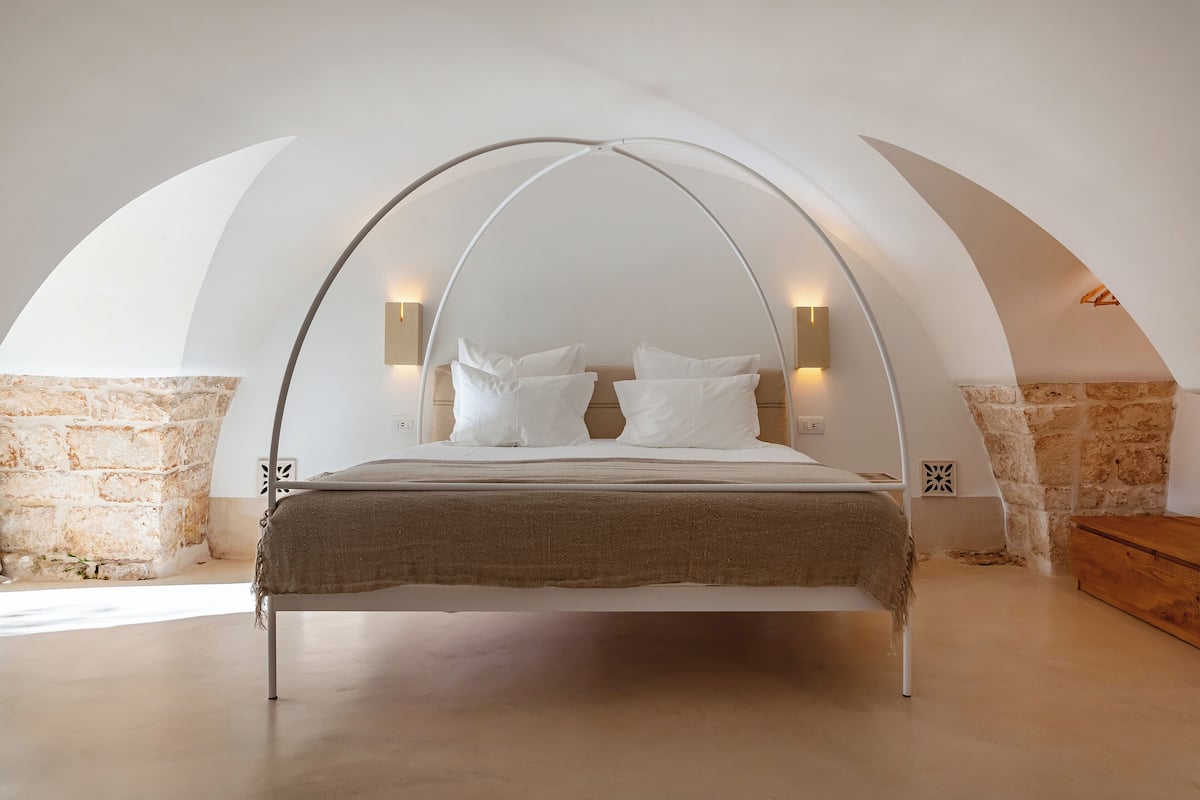 A modern bedroom with a curved ceiling, a bed with white linens, and stone walls.