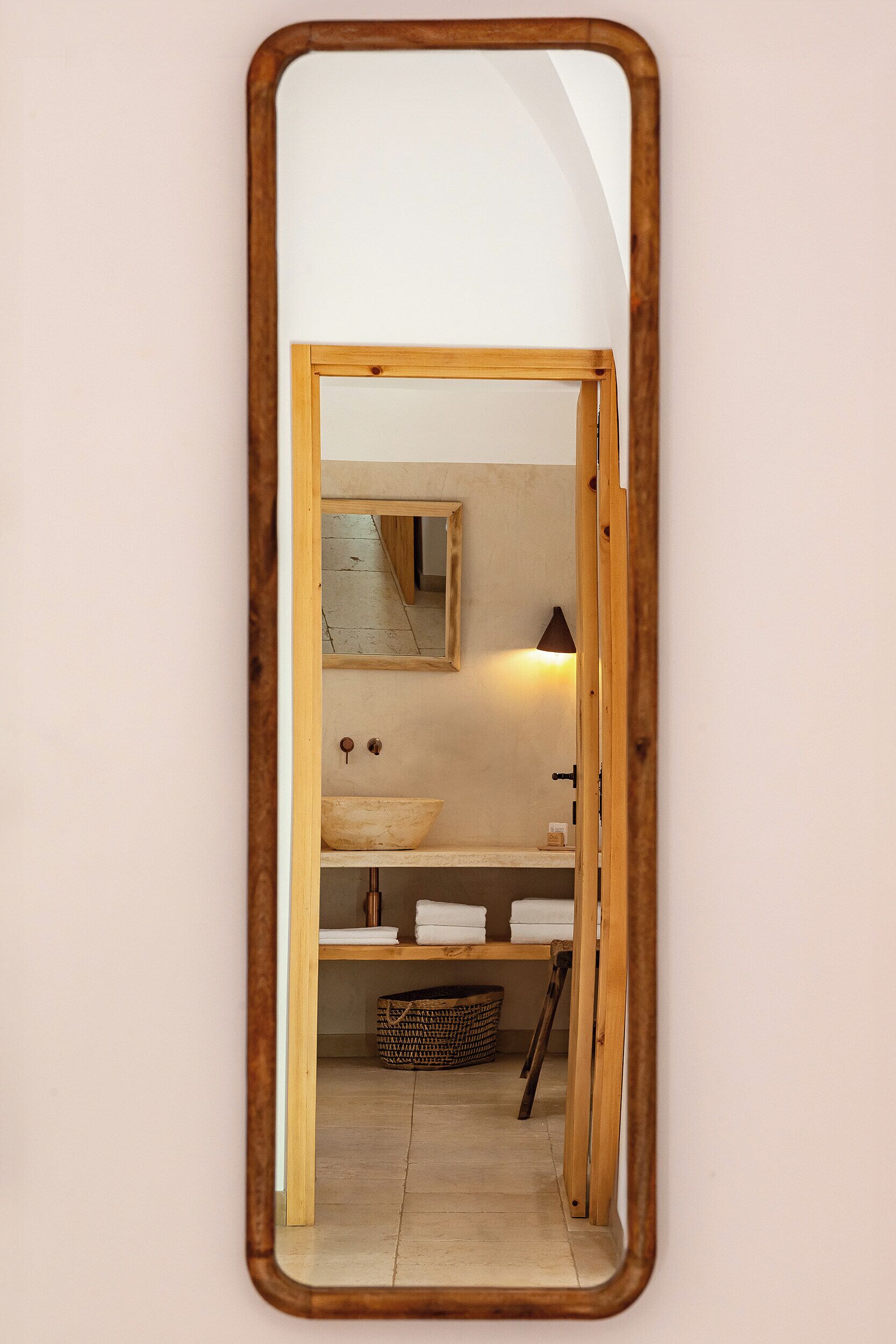 A bathroom with a wooden-framed mirror, a sink, a towel rack, and a basket.