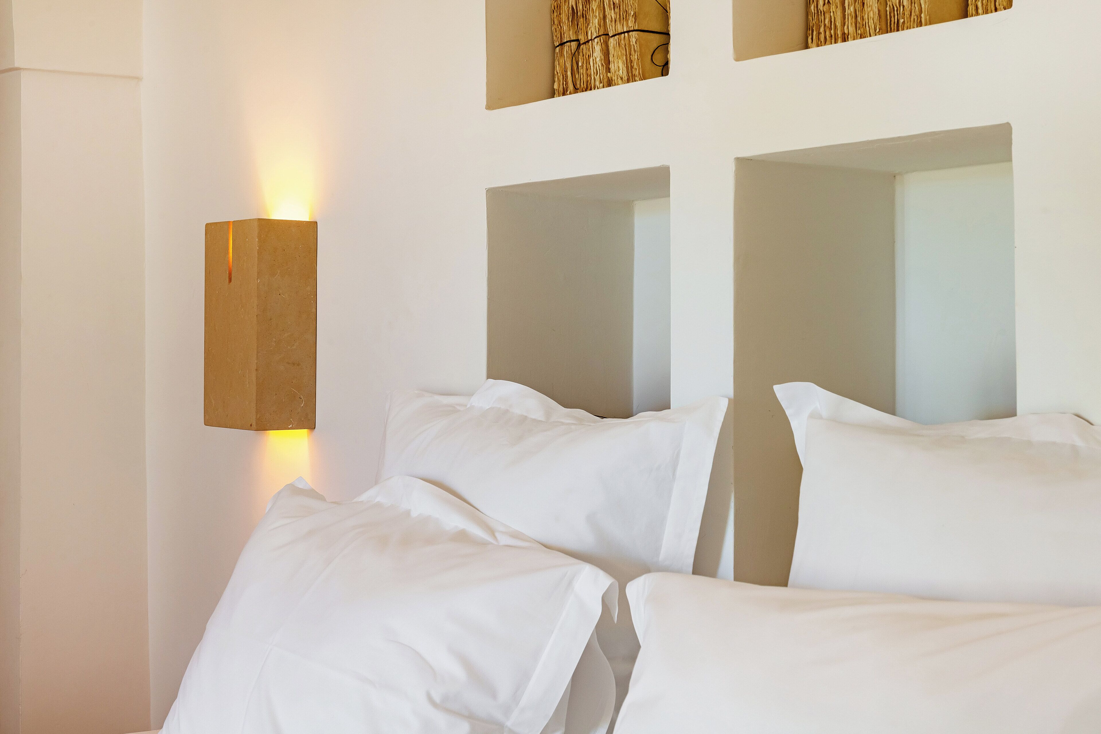 A hotel room with two beds, white bedding, and a wall-mounted light fixture.