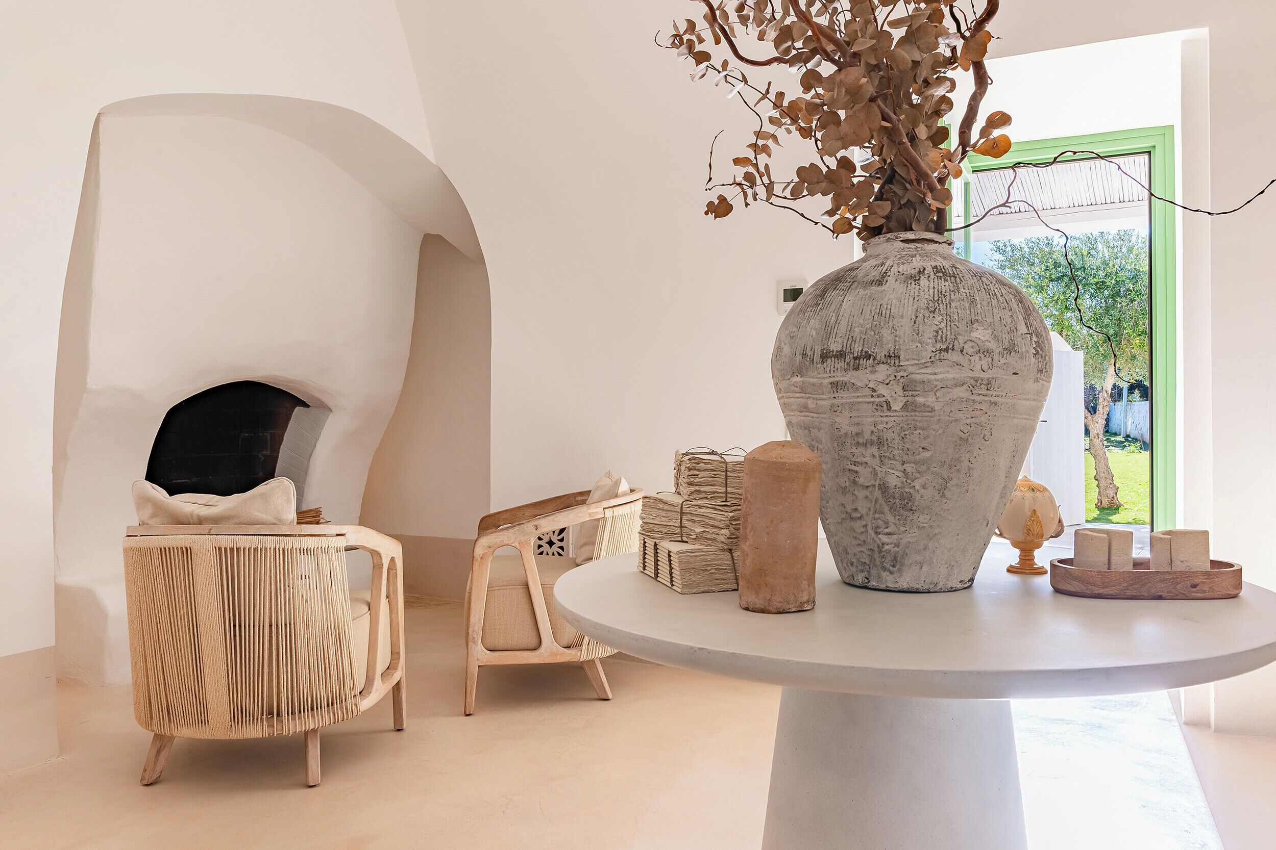 Un intérieur moderne avec une table ronde, un grand vase contenant des branches séchées et une chaise en osier.