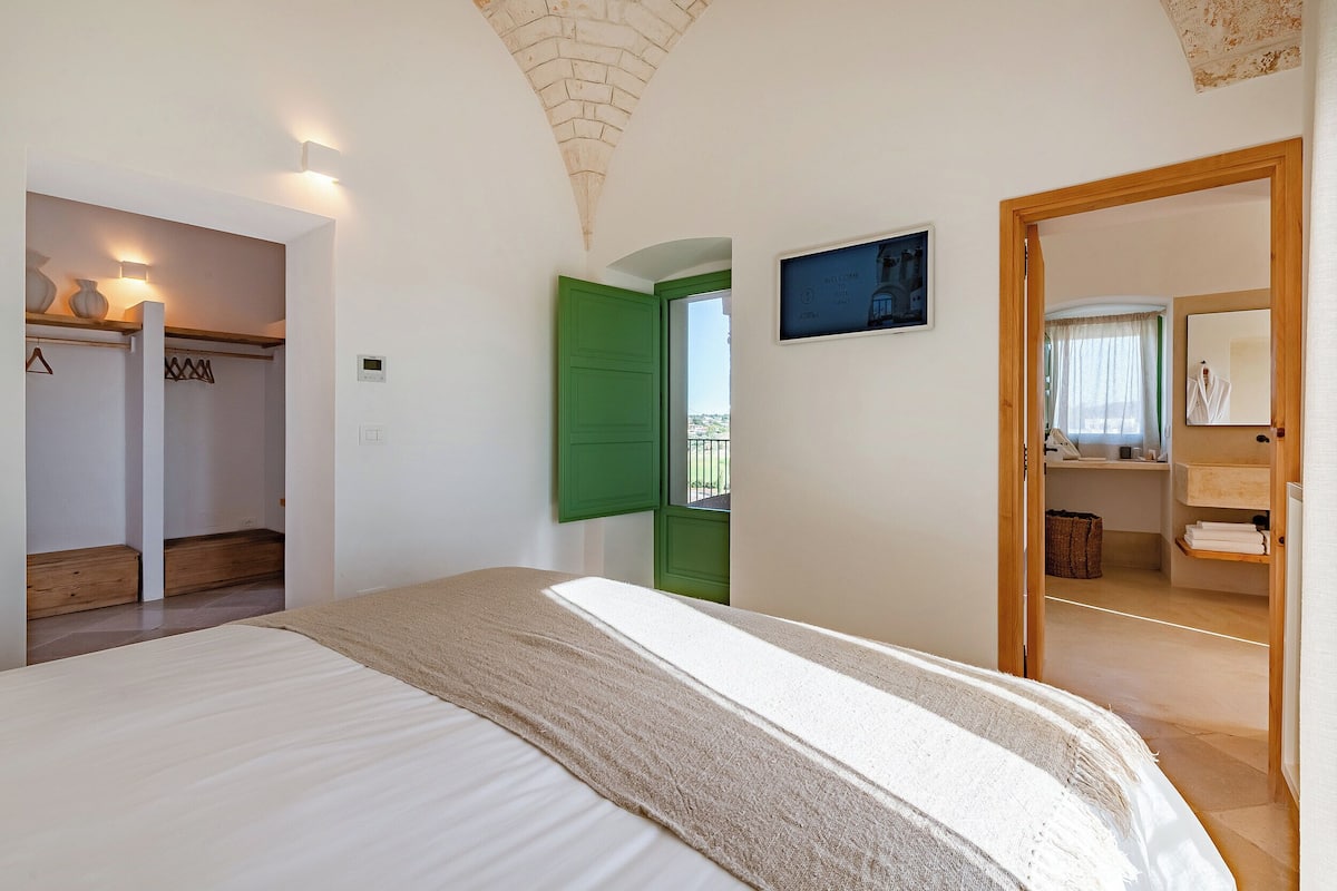 A bedroom with a bed, a green door, a welcome sign, and a view of the outside.