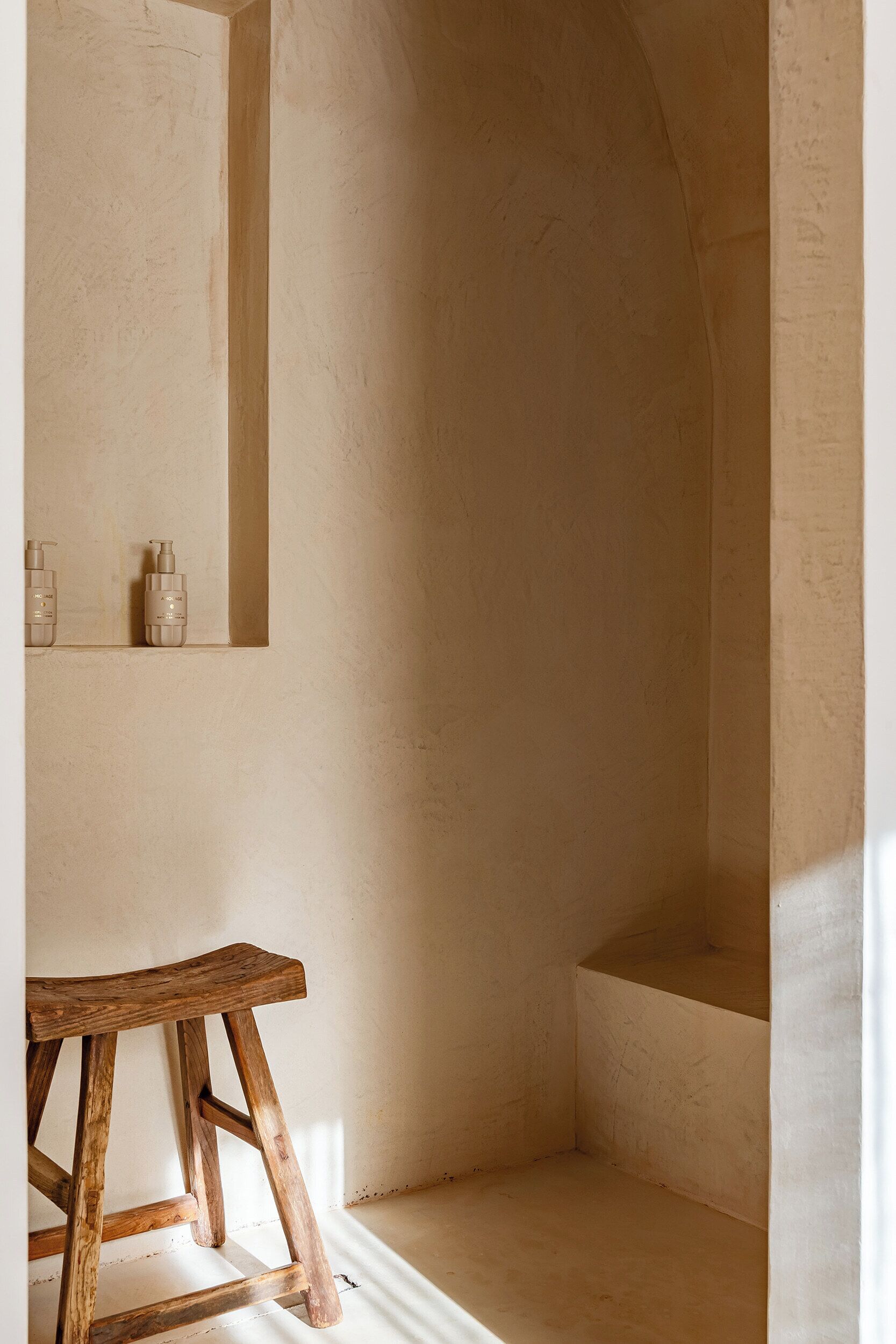 A bathroom with a wooden stool, a small shelf with toiletries, and a bathtub.