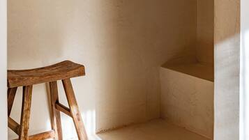 A bathroom with a wooden stool, a small shelf with toiletries, and a bathtub.