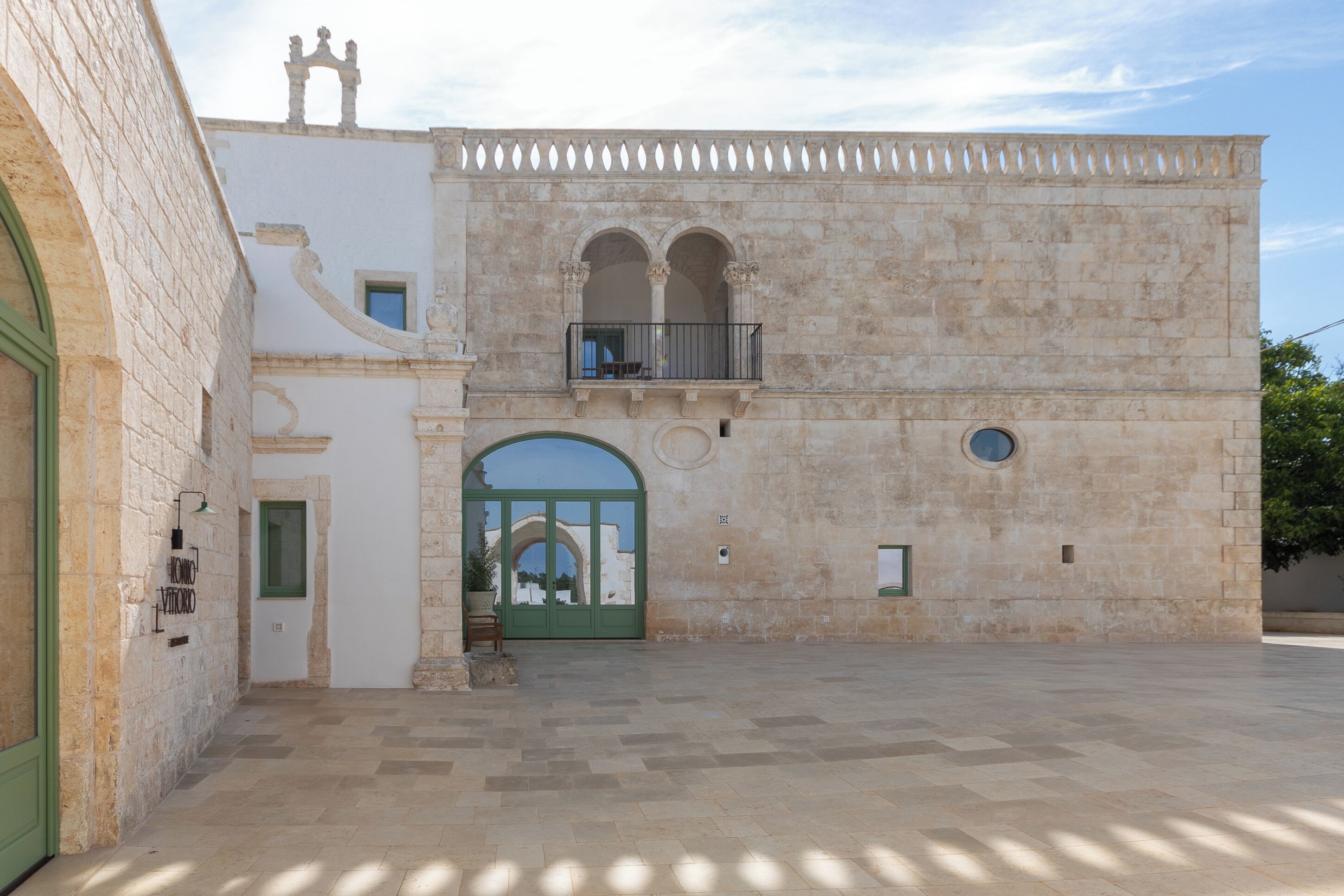 A courtyard with a stone building featuring a balcony, an arched entrance, and a small balcony with a railing.