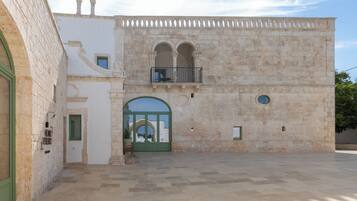 A courtyard with a stone building featuring a balcony, an arched entrance, and a small balcony with a railing.