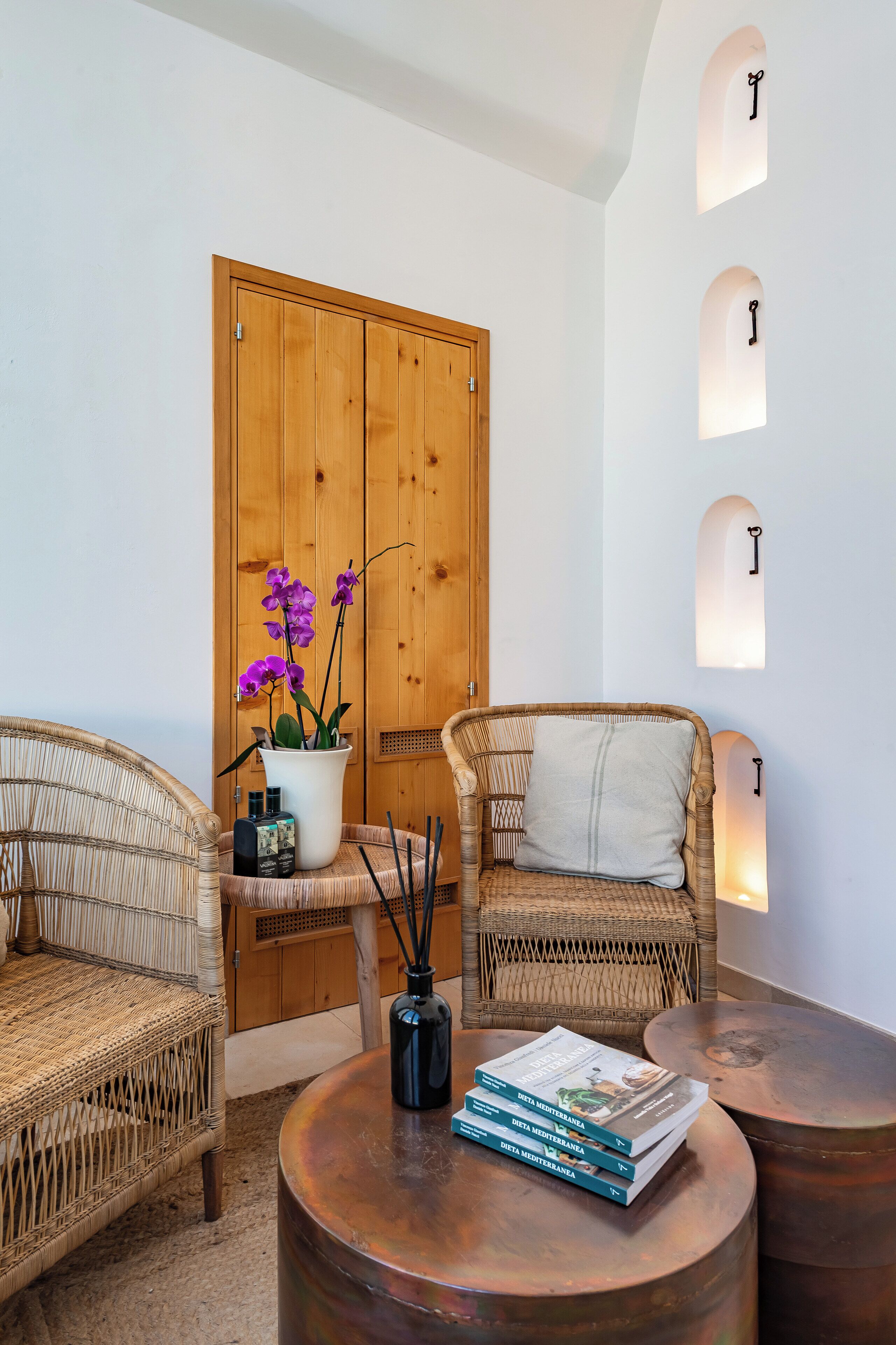 A room with wicker chairs, a wooden wardrobe, and a round table with books and a vase of flowers.