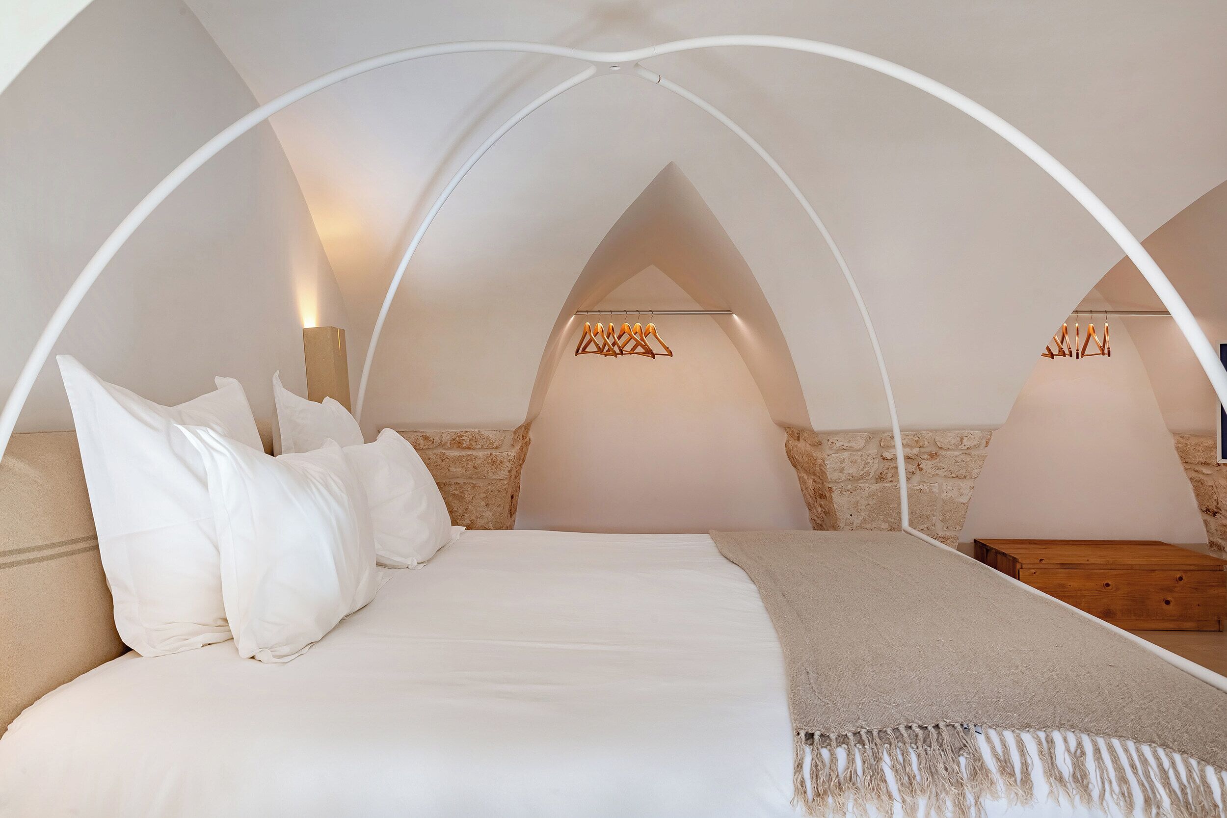 A bedroom with a vaulted ceiling, a bed with white linens, a wooden nightstand, and two wall-mounted lamps.