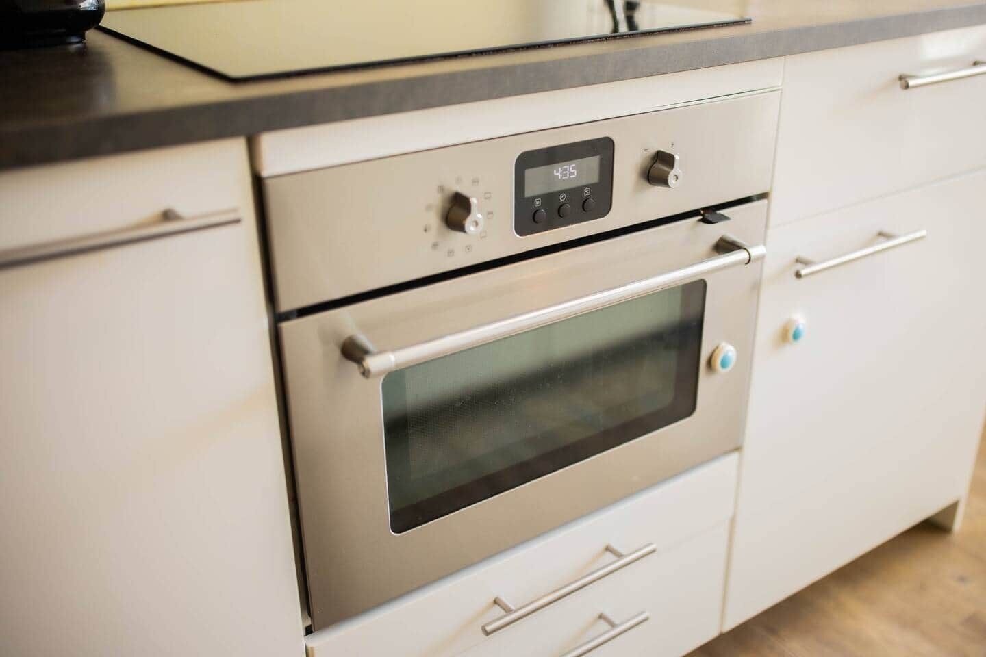 A kitchen with a stainless steel oven, a digital clock displaying 4:35, and a modern countertop.