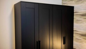 Ein großer, dunkel gefärbter Kleiderschrank mit mehreren Türen und Griffen, der an einer Wand mit einem dezenten, abstrakten Muster steht.